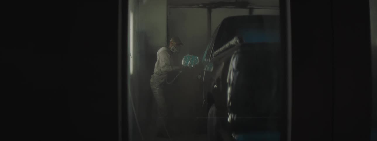 Professional using protective equipment while painting a vehicle inside a closed booth