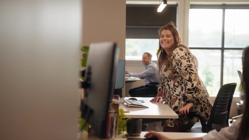 People in an office environment working in front of a computer with a woman sitting down