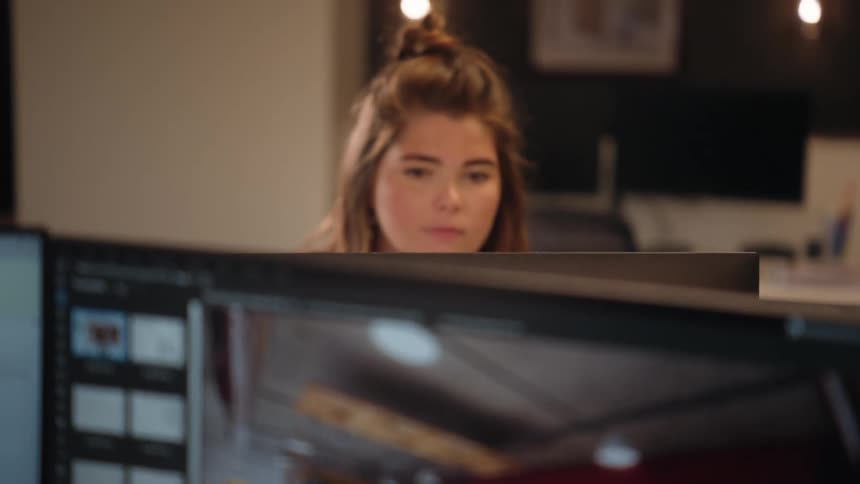 A teenage girl is seated looking intently at a computer screen displaying a restaurant interior filled with tables and chairs