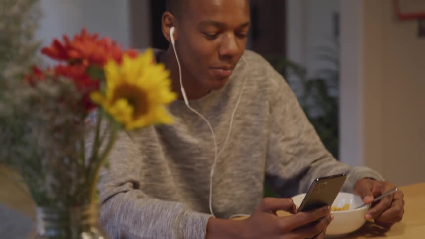 A guy eats a bowl of cereal while on his phone