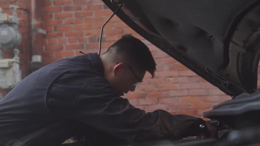Mechanic leaning over a car engine with the hood open