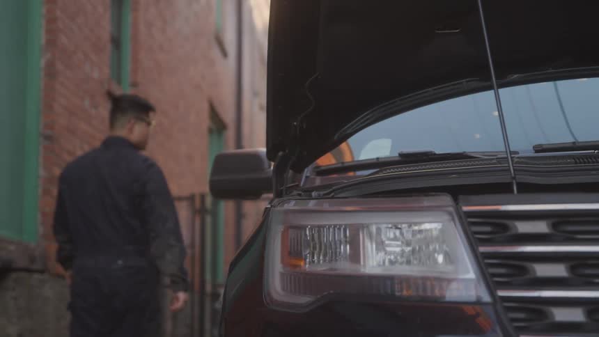 A man walks besides a car with its hood open