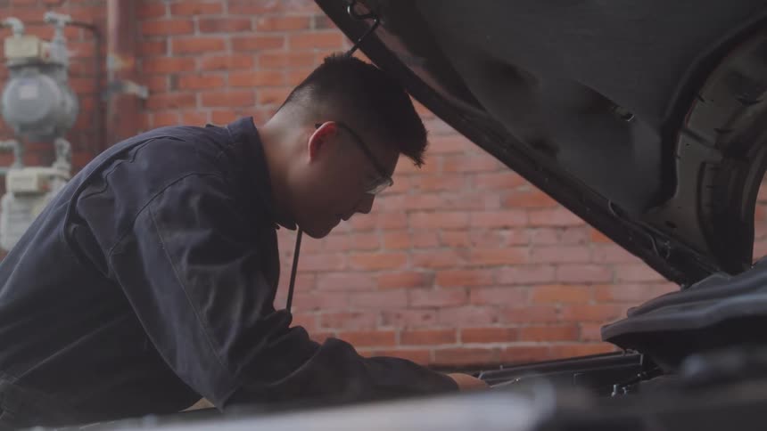 Concentrated mechanic working on a car engine with the hood open