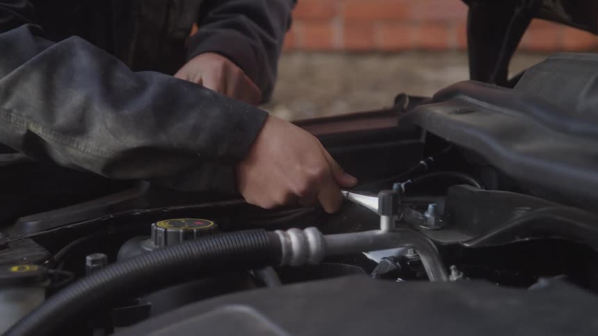 Hands of a mechanic using a wrench to adjust components in a car engine