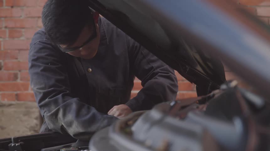 Mechanic with head down working on a car engine with the hood open