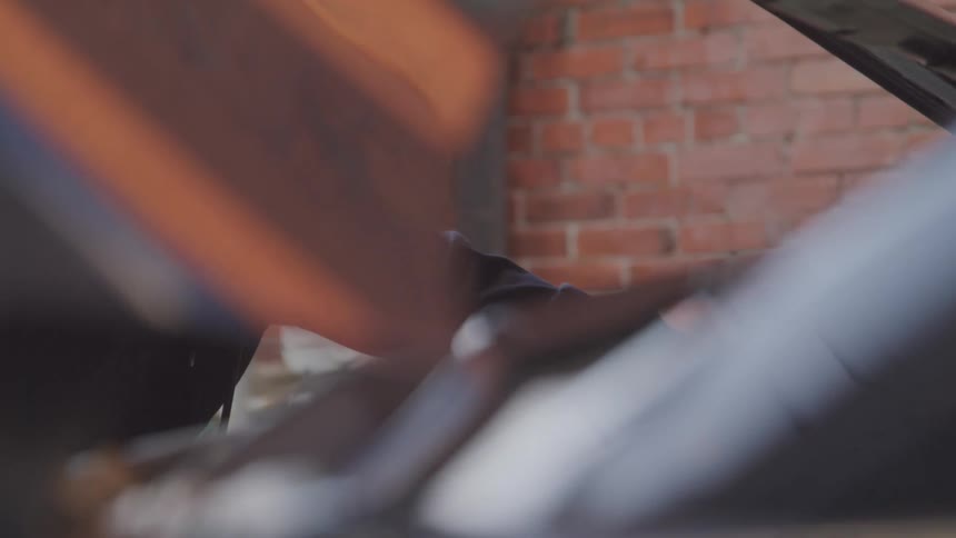 Mechanic working on a car engine with the hood open in front of a brick wall