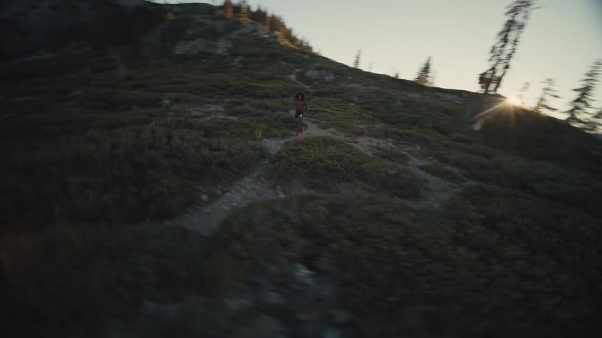 Man runs along a path in a shadowed area of mountainous terrain while the sun shines over a slope