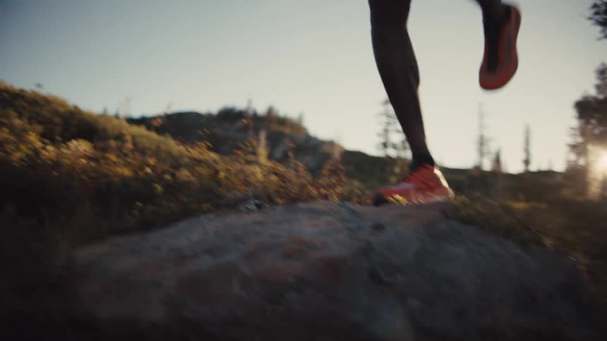 A person runs swiftly through a rocky sunlit forest landscape during golden hour
