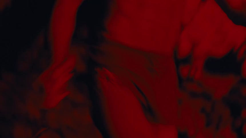 A hairy man with a flashlight stuck on his head and he is shirtless walking in an indoor environment that is all red