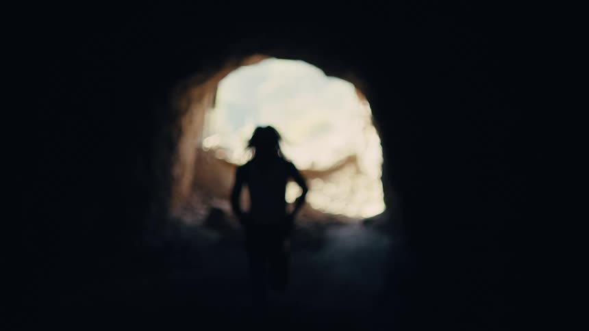 A silhouetted figure runs out of a brightly lit opening in a dark space