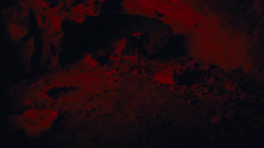A person sits on the ground inside a dark cave surrounded by intense red lighting and heavy motion blur