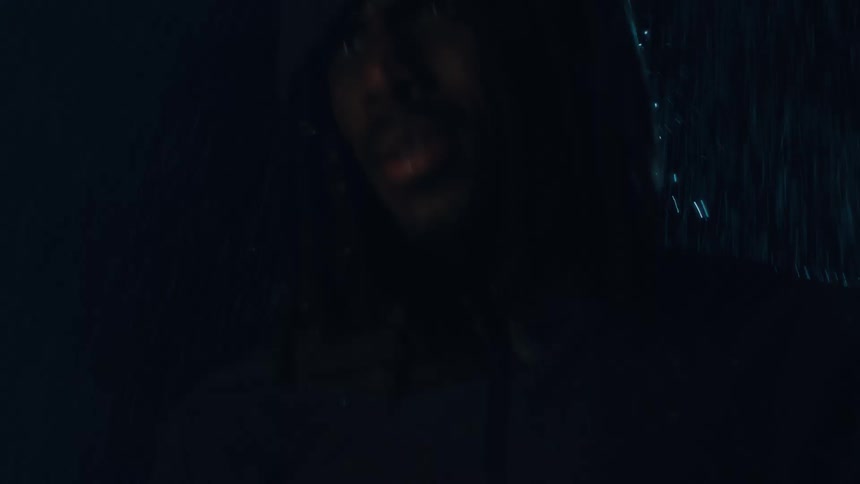 A man wearing a hooded raincoat walks through the rain in the middle of the night