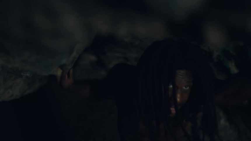 Shirtless man touches the low ceiling while making his way through a cave tunnel