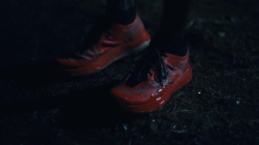 A person wearing red sneakers stands outside at night in a rain storm