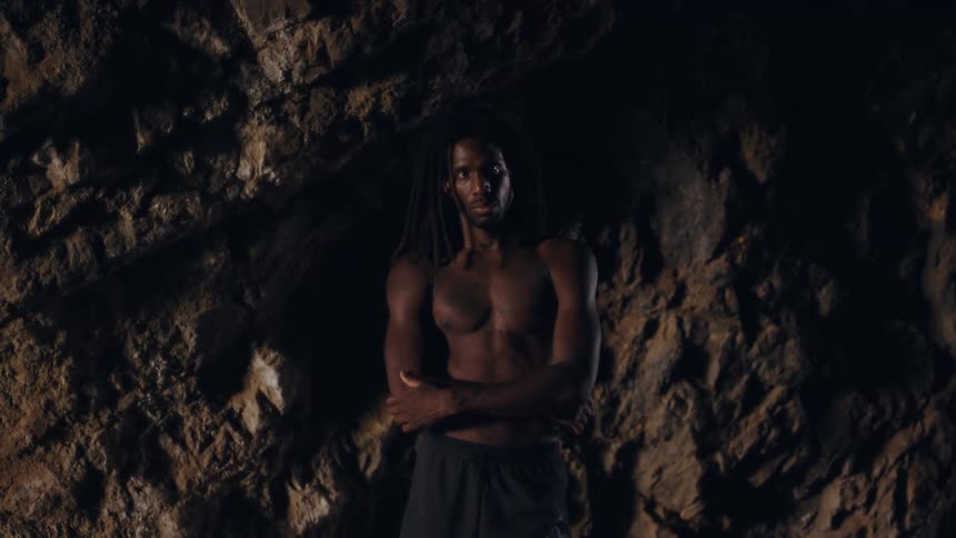 A shirtless man is standing in front of a large boulder