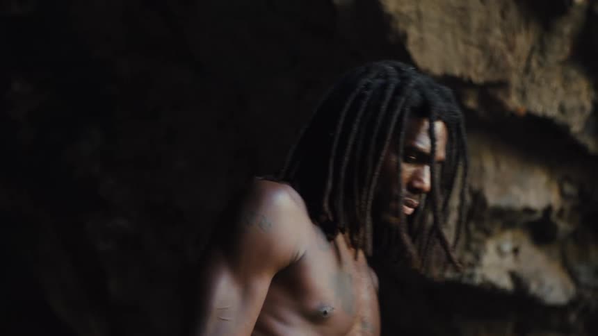 Shirtless man with dreadlocks walking in a cave