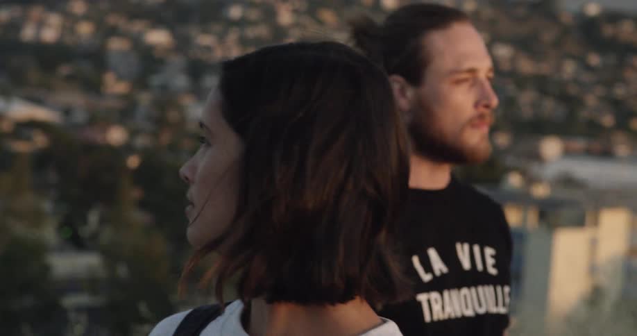 Wind blows the hair of two people standing on a hill