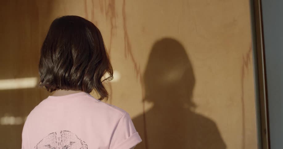 Light shines onto a person with short hair and casts her shadow on the wall