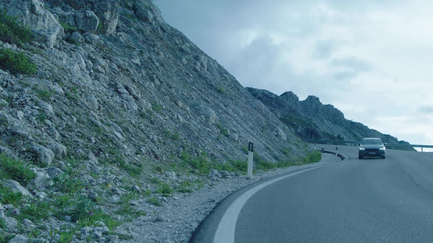 Gray vehicle traveling on a road along the edge of mountains and the sea