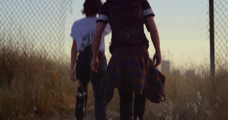 Man and woman walking through a metal fence in an outdoor setting