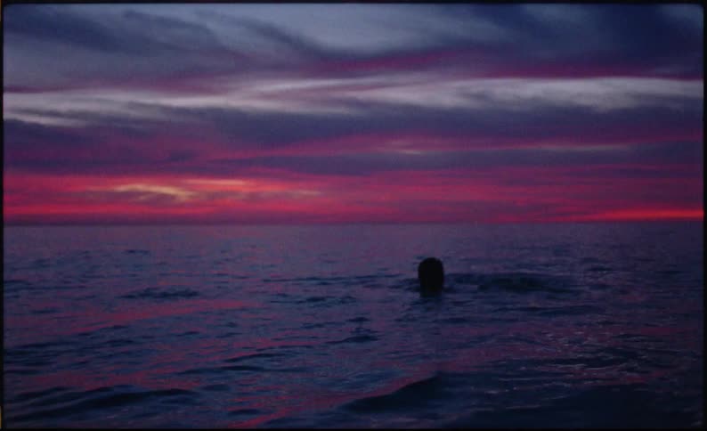 Silhouette of a person swimming in an ocean in the late afternoon with a reddish sky