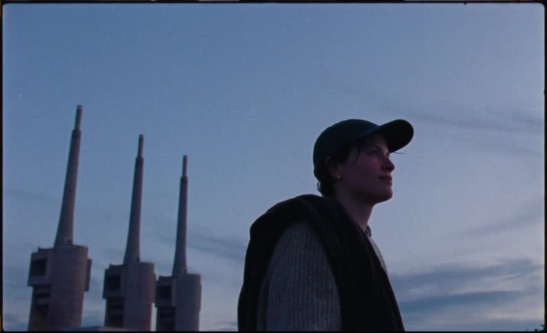 A woman adjusting her hat and smiling softly as she looks at the sky