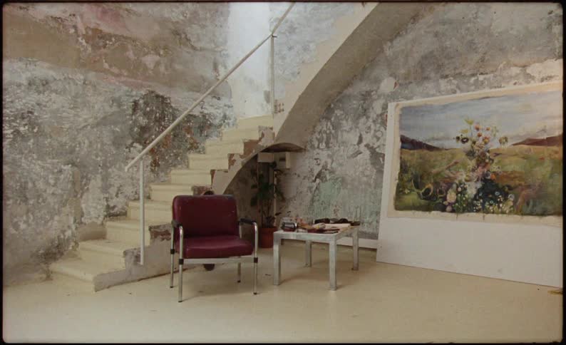 A red chair is by a big painting on the wall