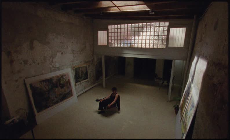A man sitting surrounded by paintings
