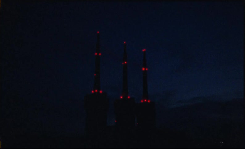 Three communication towers with red lights on against a stormy night sky