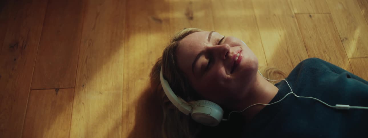 A blonde teenager lies on the floor while listening to headphones
