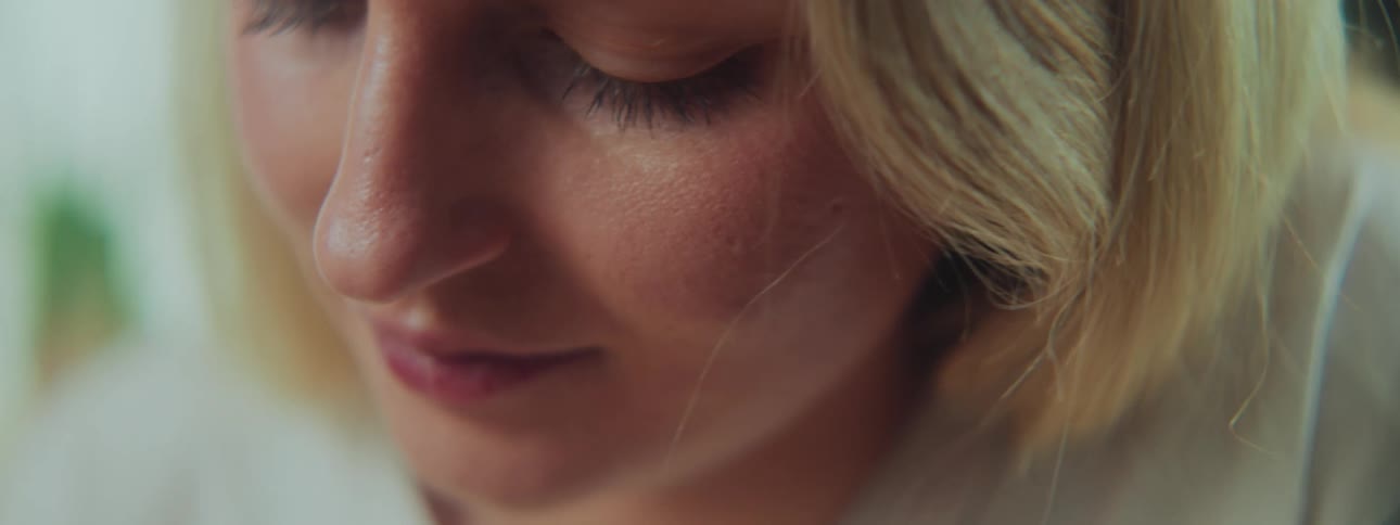 Close up of the face of a woman with blonde hair and a white shirt looking down