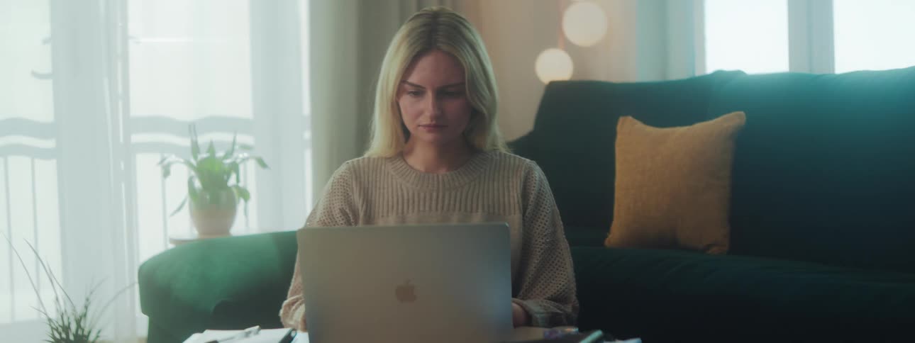 A woman works on a laptop while seated on the floor in a room