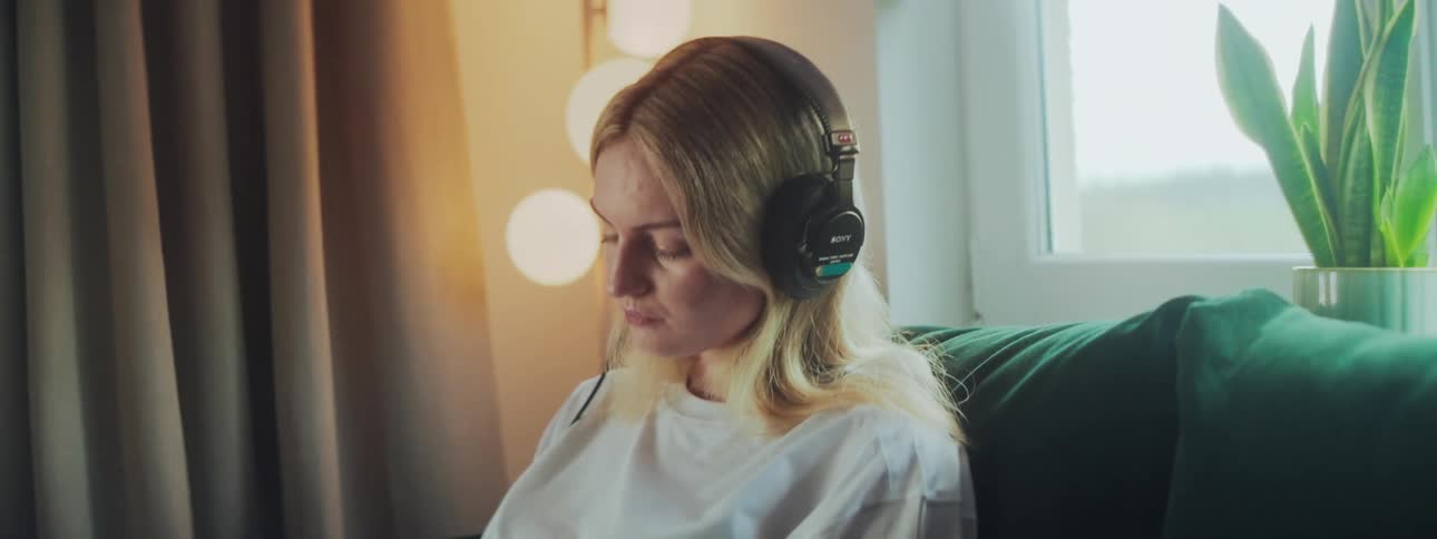 A woman wearing headphones uses a stylus on a tablet while seated indoors