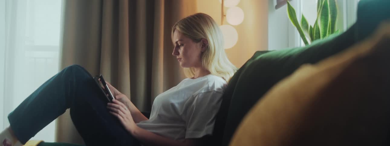 A woman is sitting on the couch using her tablet