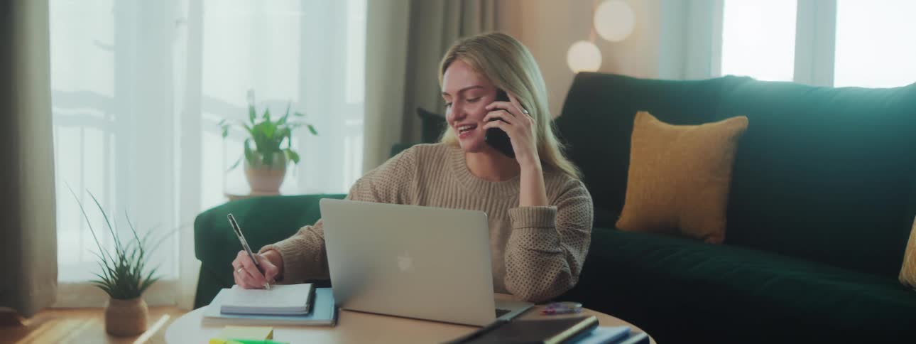 Blonde woman talking on cell phone and facing laptop