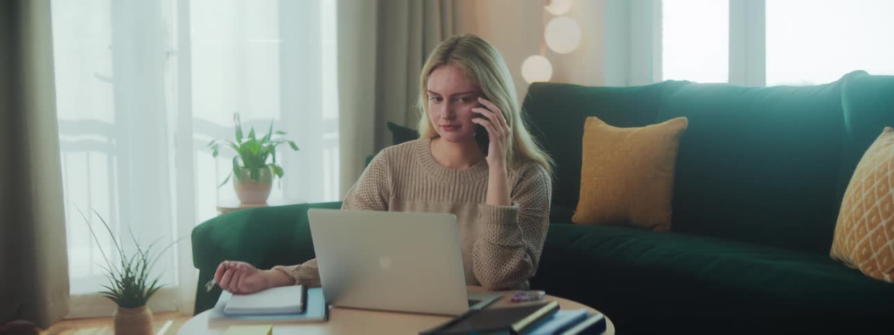 A young woman sits on her living room floor and talks on a smartphone