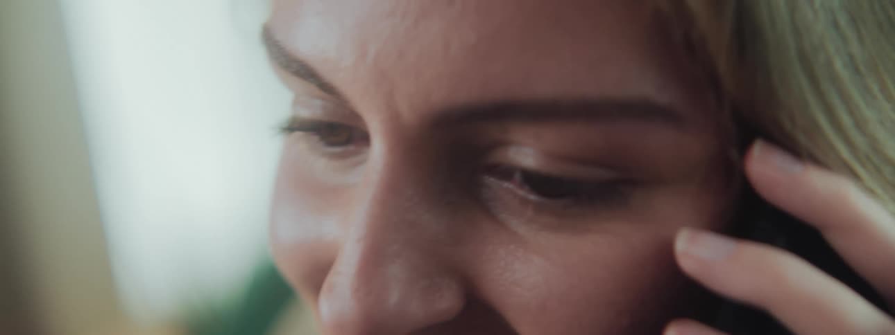 A close up of the face of a blonde woman talking on a smartphone in a room