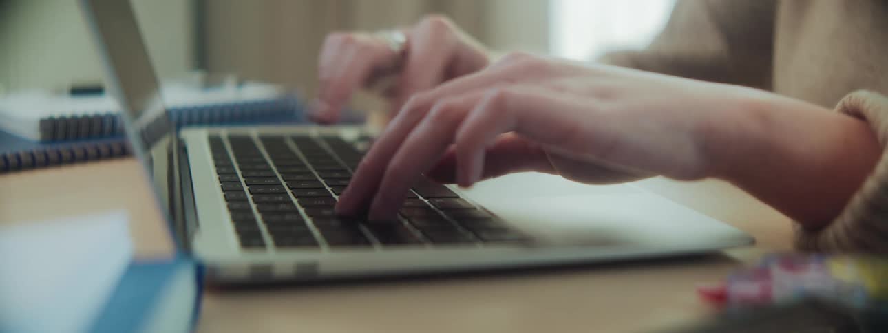 Hands typing on a laptop keyboard surrounded by a notebook pen and other workspace essentials