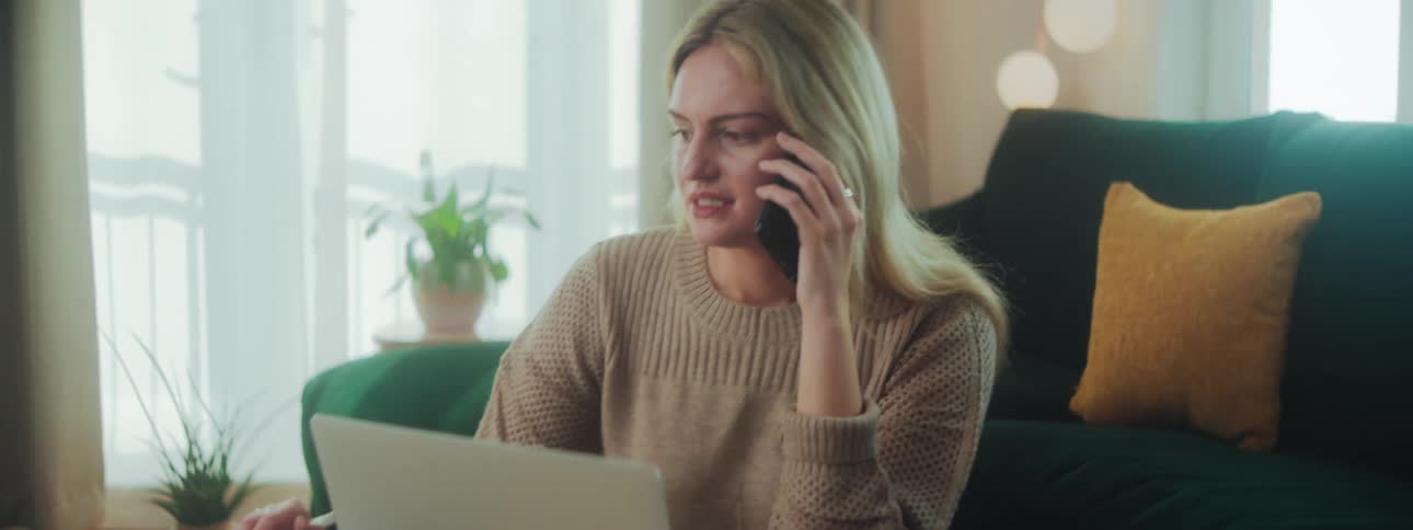 A woman is writing in a notebook while talking on her phone