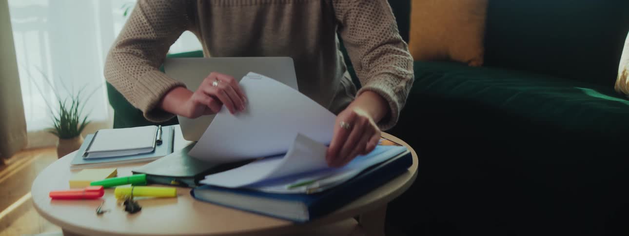 A woman picks up a paper by the laptop