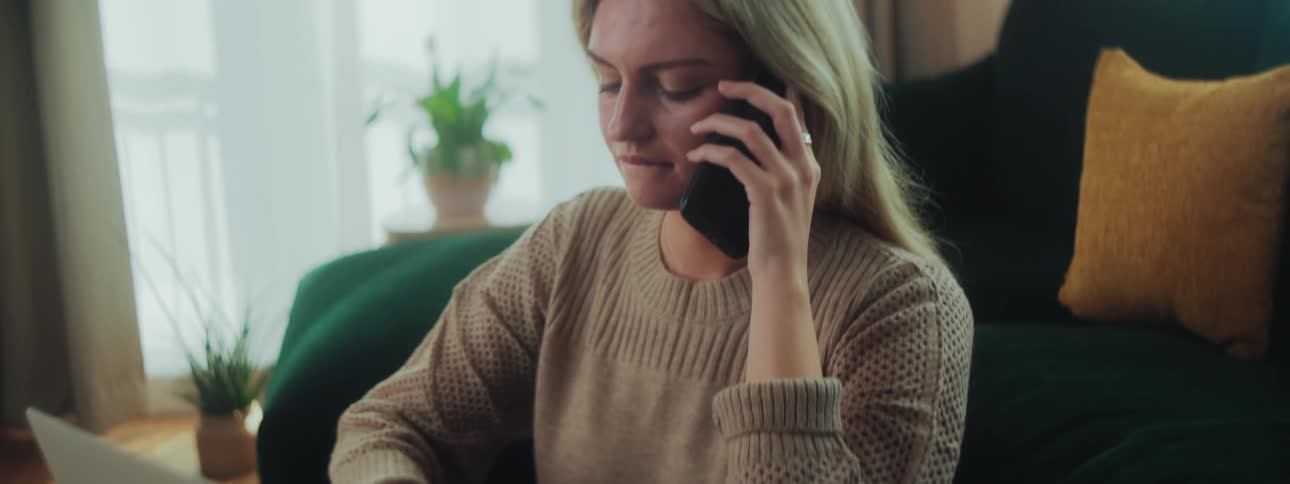 A woman in a room listening on the phone and typing on her laptop