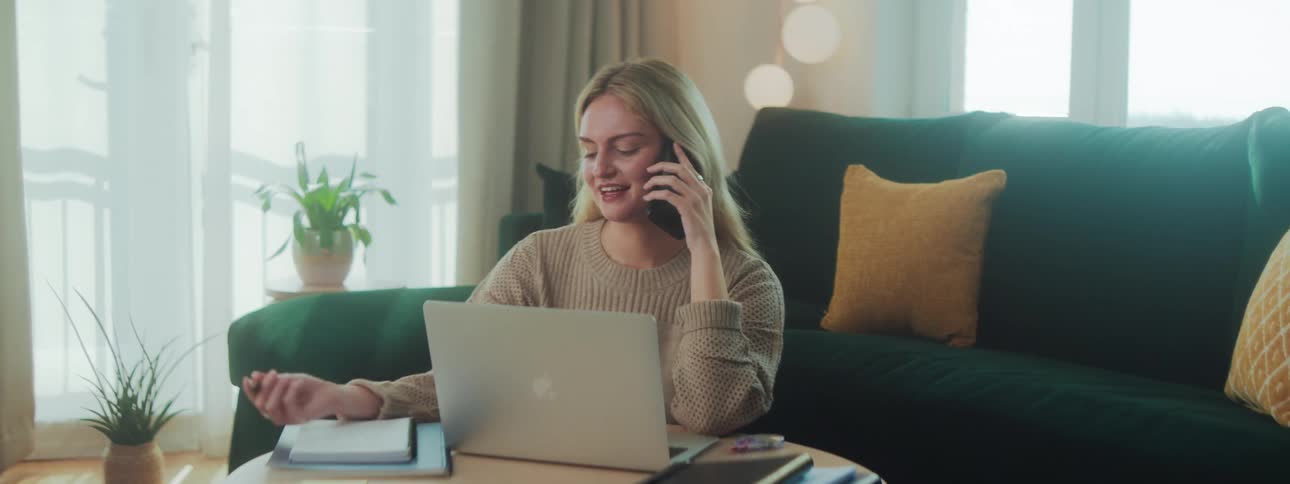 A woman smiles while talking on her cell phone and writing in a notebook