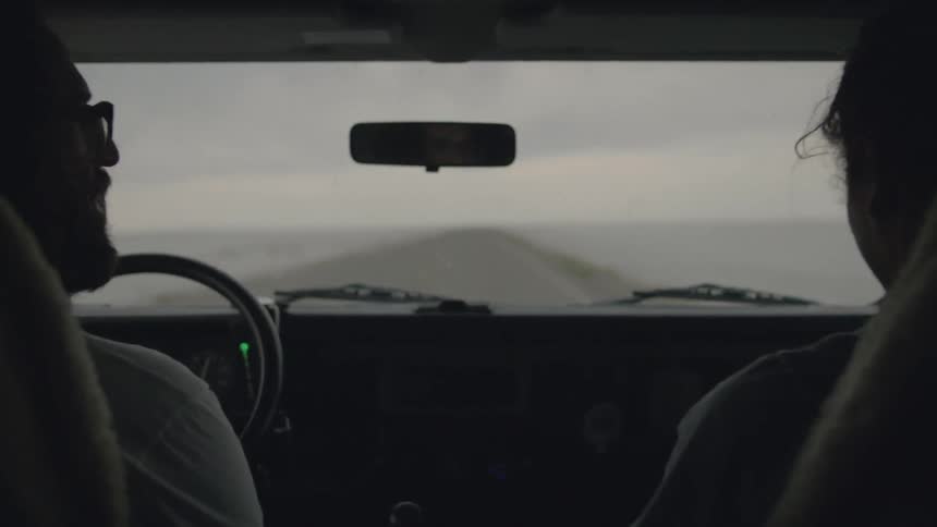 Man driving a vehicle and gesturing to his friend