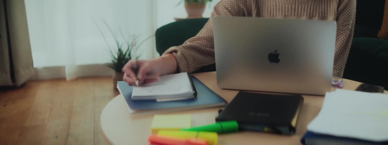 A woman works on a laptop and writes in a notebook while seated on the floor