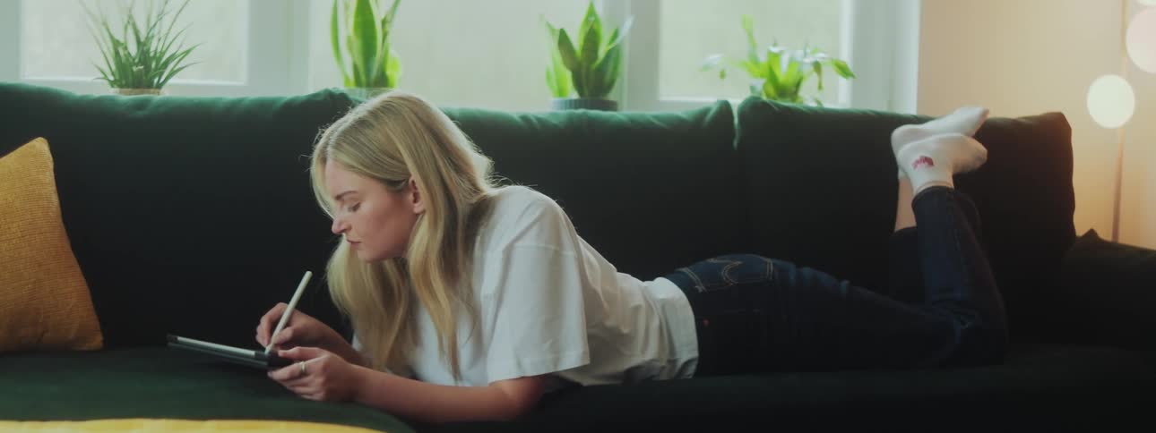 Woman lying face down on sofa writing