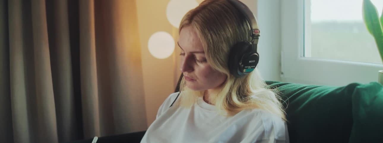 Woman with headphones sitting on the couch drawing on a tablet