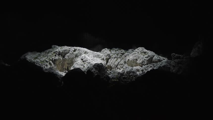 A circle of light moves from top to bottom illuminating a pile of rocks at night