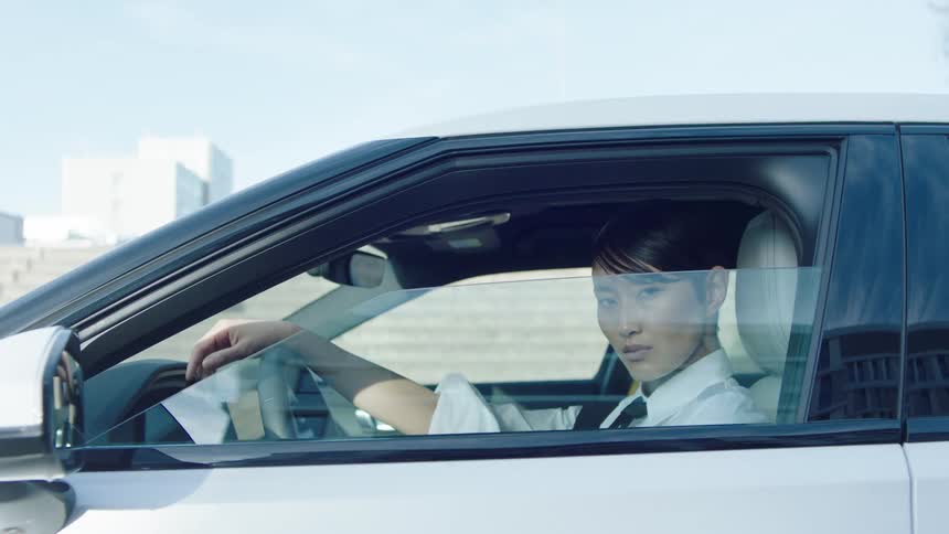 Asian man rolls up his window while sitting in the driver seat of a car
