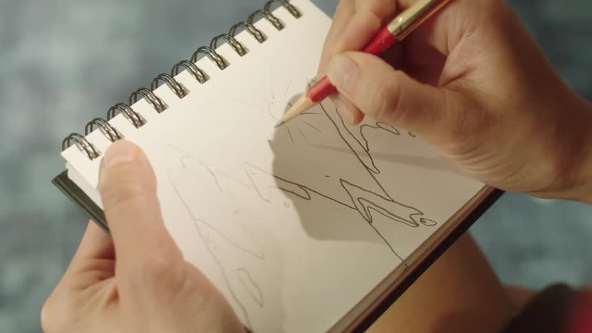 A person drawing the sun in a sketchbook with a pencil