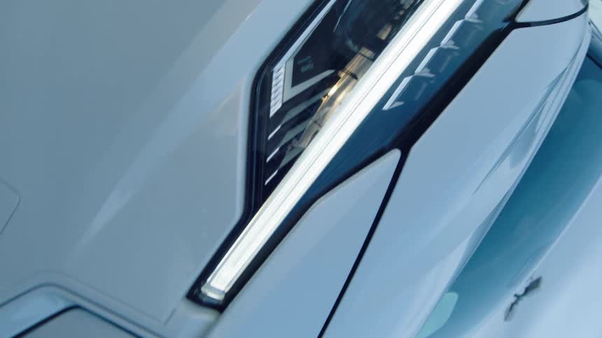 A close up shot shows the illuminated headlight of a white vehicle